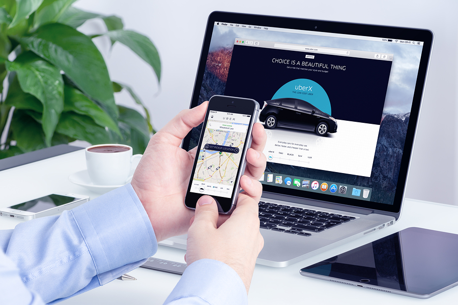Varna Bulgaria - May 29 2015: Man orders Uber X through his iPhone and Macbook with Uber website on the background. Uber Technologies Inc. is an American international transportation network company.