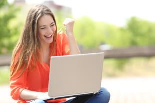 Euphoric woman searching job with a laptop in an urban park in summer
