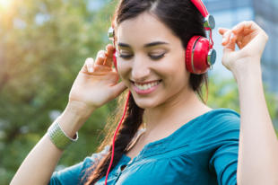 Closeup shot of young woman listening to music in a park. Portrait of happy smiling girl feeling free with music. Close up of latin girl listening to music with headphone and dancing in a city center.