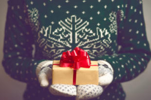 Girl holds in hands Christmas present. Christmas background. Gifts for men. Knitted mittens. Knitted dress. 2017 year. Box with gifts. Merry Christmas. Toned image.