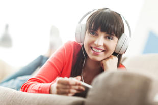 Smiling young woman relaxing at home on the couch she is wearing headphones using a digital tablet and watching a streaming video