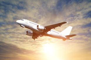 Airplane closeup - travel background with airplane flying in the colored sunny sky. White flying airplane in the sunlight - closeup of flying airplane with blank livery.Airplane in the flight
